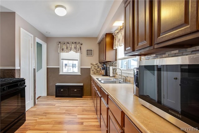 kitchen featuring black range with gas stovetop, light hardwood / wood-style flooring, tasteful backsplash, and sink