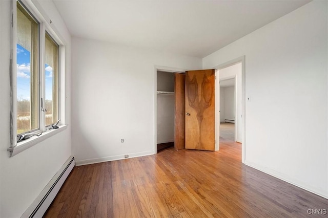 unfurnished bedroom featuring a closet, baseboard heating, and light hardwood / wood-style floors