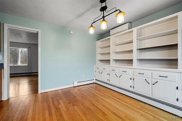 unfurnished living room with baseboard heating, a wall unit AC, and light hardwood / wood-style flooring