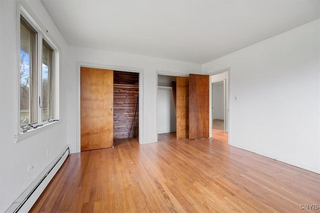 unfurnished bedroom featuring light hardwood / wood-style floors, two closets, and a baseboard radiator