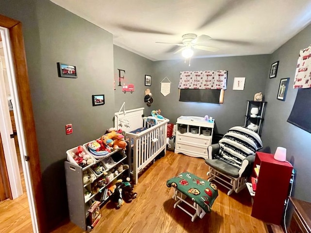 bedroom with a nursery area, ceiling fan, and hardwood / wood-style flooring