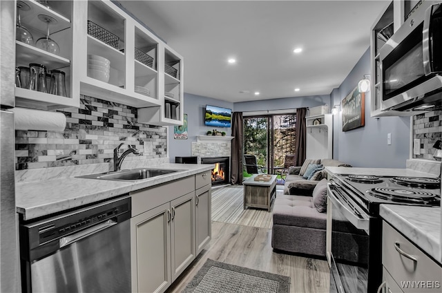 kitchen with sink, appliances with stainless steel finishes, light stone counters, light hardwood / wood-style floors, and a stone fireplace