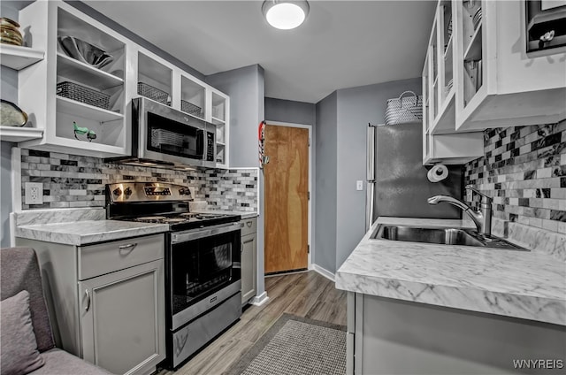 kitchen featuring sink, light hardwood / wood-style flooring, decorative backsplash, gray cabinets, and appliances with stainless steel finishes