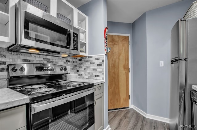 kitchen featuring light stone counters, stainless steel appliances, light hardwood / wood-style floors, and backsplash