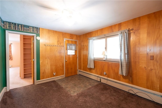 carpeted empty room with wood walls and a baseboard radiator