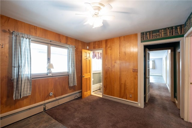 empty room with ceiling fan, a baseboard radiator, dark carpet, and wooden walls