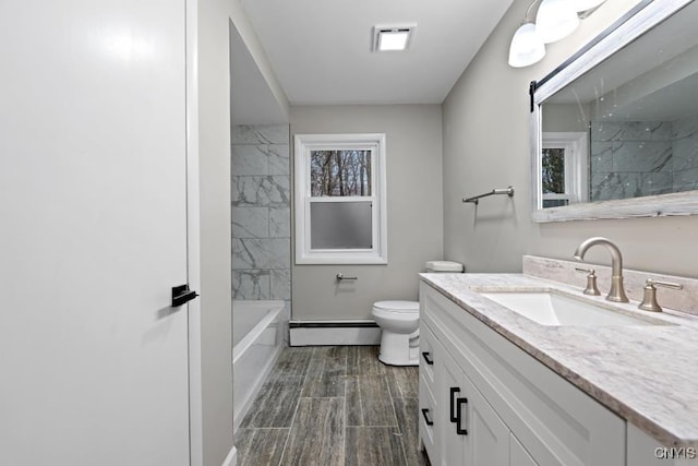 full bathroom featuring toilet, vanity, a baseboard heating unit, and tiled shower / bath