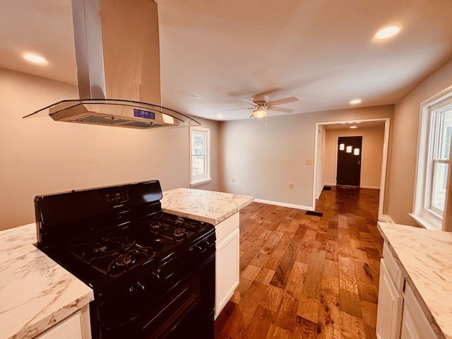 kitchen featuring island exhaust hood, gas stove, white cabinets, ceiling fan, and wood-type flooring