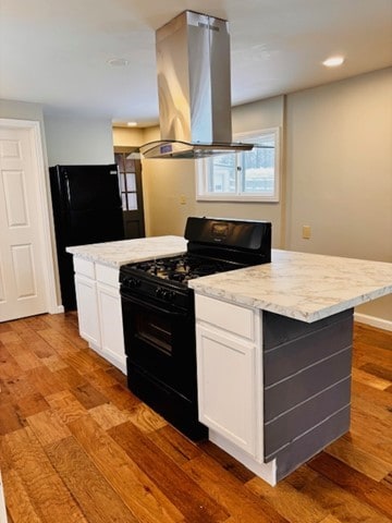 kitchen with white cabinets, black appliances, island range hood, and light hardwood / wood-style flooring