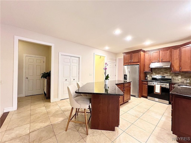 kitchen featuring stainless steel appliances, a center island, light tile patterned floors, dark stone counters, and backsplash