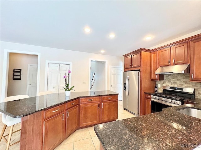 kitchen with dark stone countertops, decorative backsplash, a kitchen island, appliances with stainless steel finishes, and light tile patterned flooring