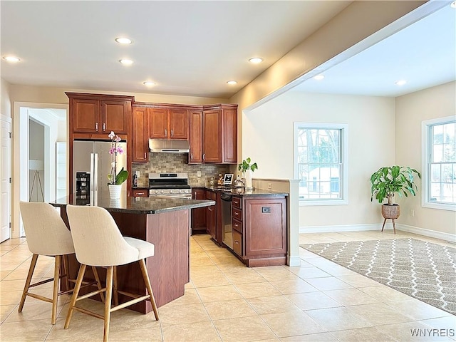 kitchen with a breakfast bar, light tile patterned floors, backsplash, dark stone counters, and appliances with stainless steel finishes