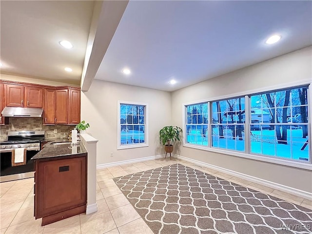 kitchen featuring stainless steel gas stove, kitchen peninsula, light tile patterned floors, decorative backsplash, and sink