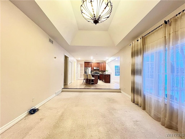 corridor featuring a chandelier, a tray ceiling, and light colored carpet