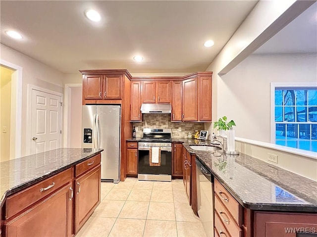 kitchen with stainless steel appliances, dark stone countertops, light tile patterned flooring, and sink