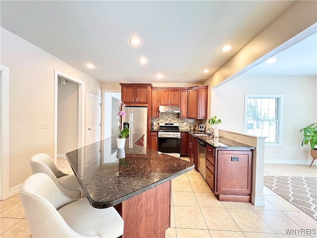 kitchen featuring kitchen peninsula, tasteful backsplash, a kitchen bar, appliances with stainless steel finishes, and light tile patterned flooring