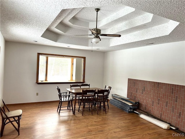 dining area with hardwood / wood-style floors, a tray ceiling, a textured ceiling, and ceiling fan