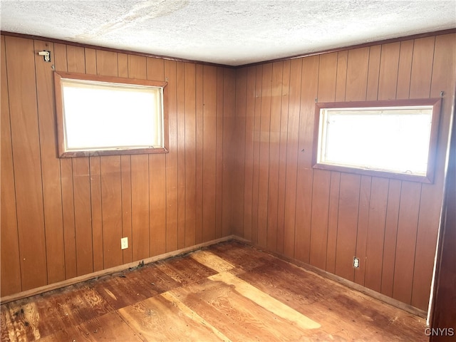 unfurnished room with wood-type flooring, wooden walls, and a textured ceiling