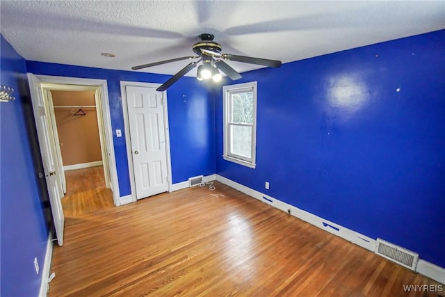 unfurnished bedroom featuring a closet, wood-type flooring, a textured ceiling, and ceiling fan