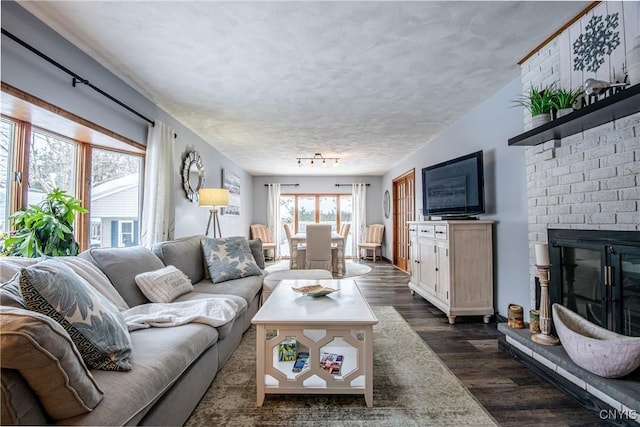 living room with dark hardwood / wood-style floors, a textured ceiling, and a brick fireplace