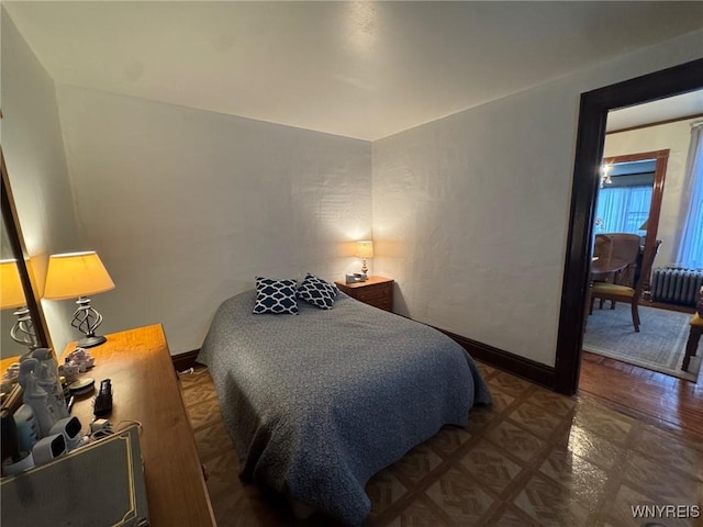 bedroom with dark parquet flooring, radiator heating unit, and multiple windows