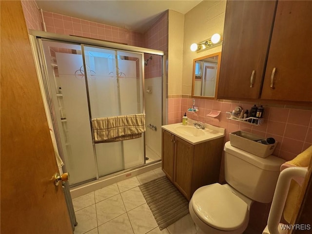 bathroom with toilet, vanity, tile walls, tile patterned floors, and a shower with door