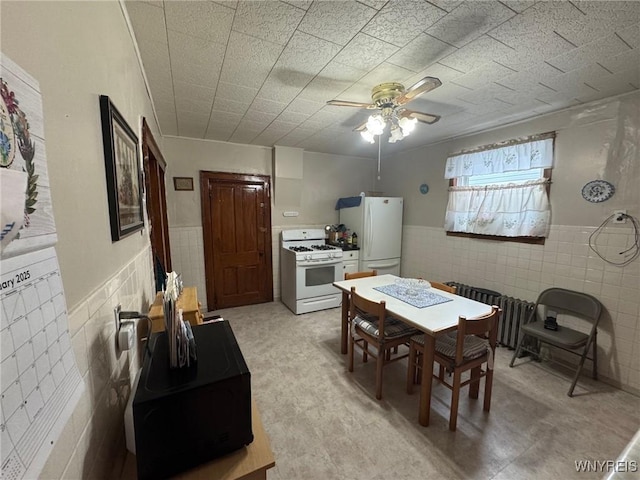 dining room featuring ceiling fan and tile walls