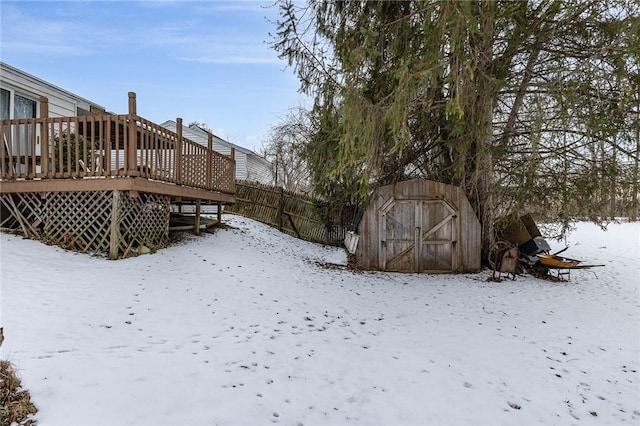 yard layered in snow featuring a deck and a storage shed