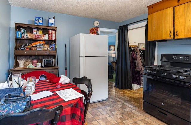 kitchen featuring black gas range, white refrigerator, and a textured ceiling