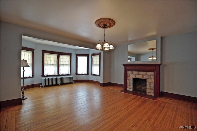 unfurnished living room featuring radiator, a fireplace, a chandelier, and hardwood / wood-style floors