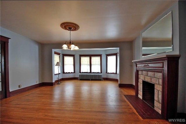 unfurnished living room with a notable chandelier, wood-type flooring, a stone fireplace, and radiator heating unit