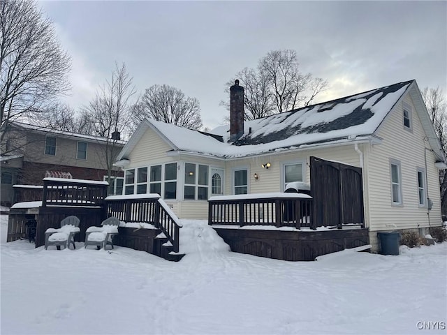 snow covered back of property featuring a deck and a sunroom