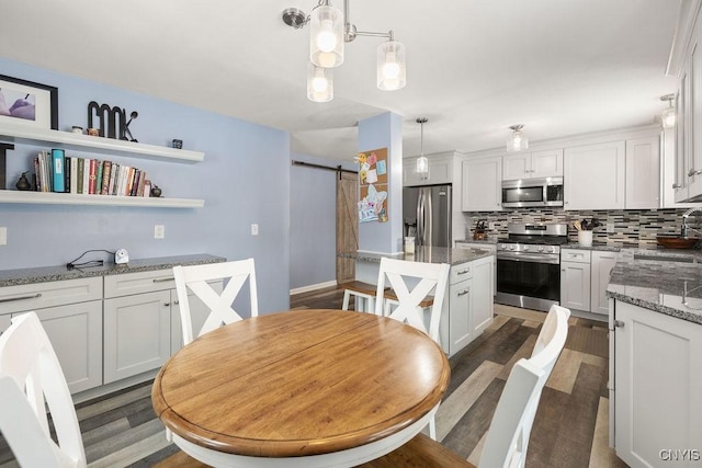 kitchen featuring decorative light fixtures, white cabinets, stainless steel appliances, and a barn door