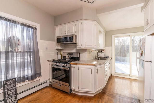 kitchen with appliances with stainless steel finishes, a baseboard radiator, white cabinets, light hardwood / wood-style flooring, and sink