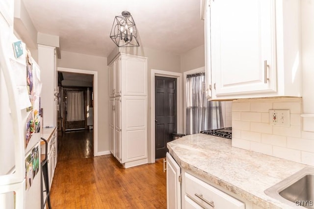 kitchen with a notable chandelier, pendant lighting, wood-type flooring, decorative backsplash, and white cabinetry