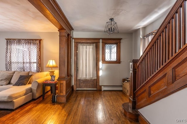 foyer featuring a baseboard radiator, wood-type flooring, ornate columns, and a chandelier