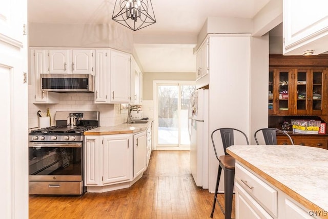 kitchen featuring white cabinetry, appliances with stainless steel finishes, decorative light fixtures, a chandelier, and sink