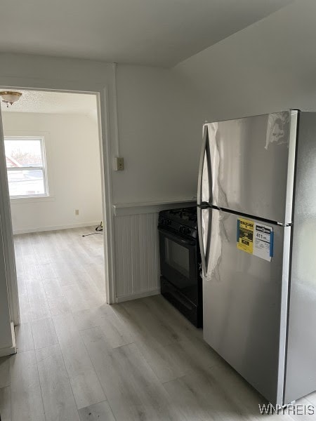 kitchen featuring white cabinetry, gas stove, light wood-type flooring, and stainless steel fridge