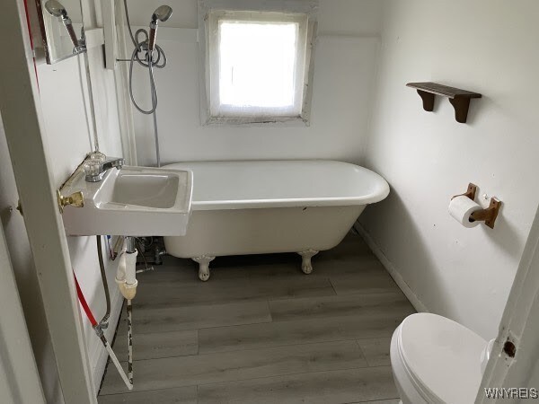 bathroom featuring hardwood / wood-style flooring, sink, toilet, and a tub to relax in