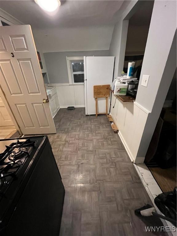 kitchen featuring white cabinets, white fridge, parquet flooring, and black gas stove