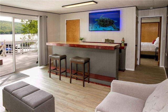 bar featuring butcher block countertops, wood walls, a water view, and light wood-type flooring