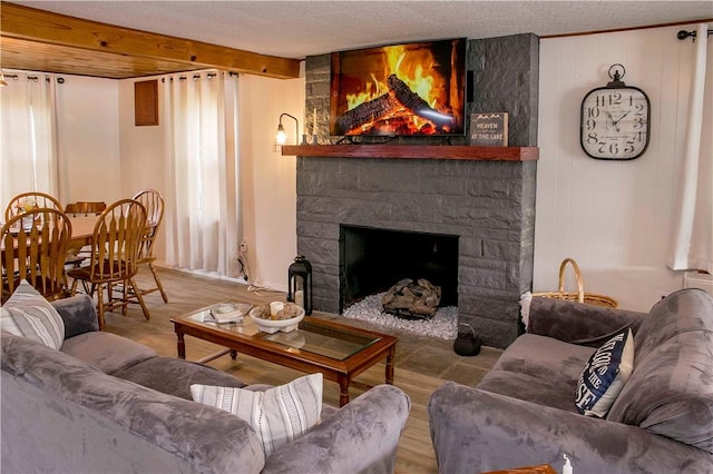 living room with a textured ceiling, light hardwood / wood-style flooring, a stone fireplace, and beamed ceiling