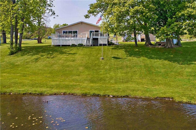 rear view of house featuring a deck with water view and a lawn