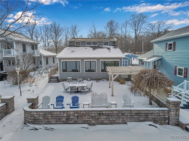 snow covered back of property with a pergola