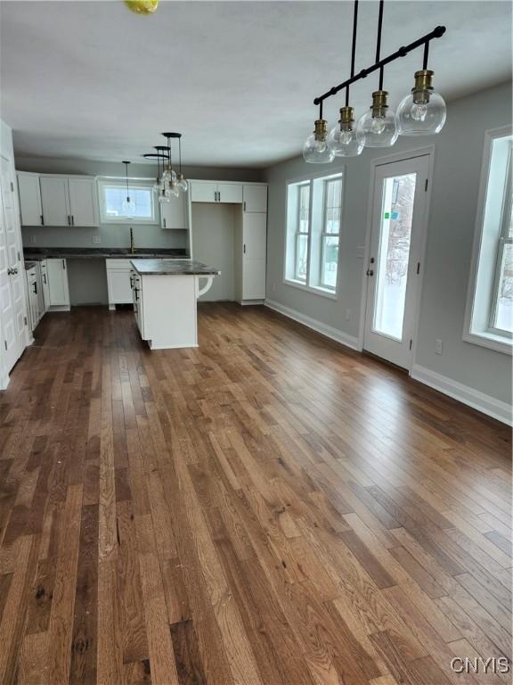 kitchen with decorative light fixtures, dark hardwood / wood-style floors, a center island, sink, and white cabinets