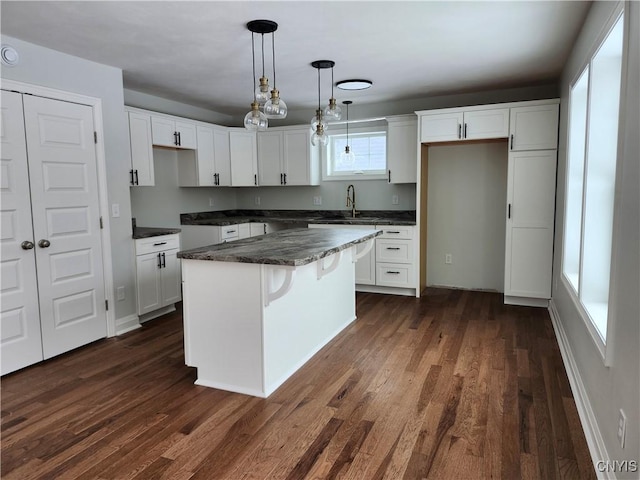 kitchen with hanging light fixtures, dark wood-type flooring, white cabinetry, and a kitchen island