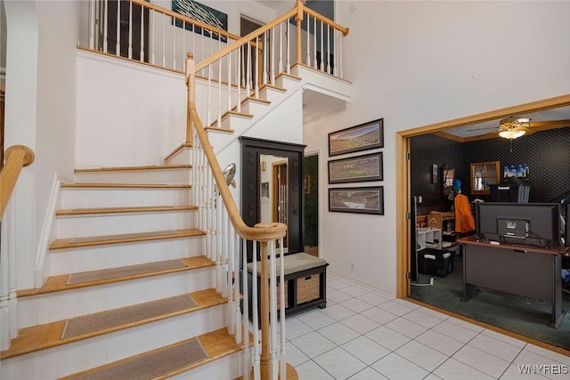 stairway with ceiling fan, tile patterned flooring, and a towering ceiling