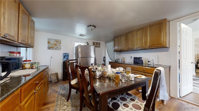 kitchen featuring dark stone countertops, light hardwood / wood-style flooring, and stainless steel refrigerator