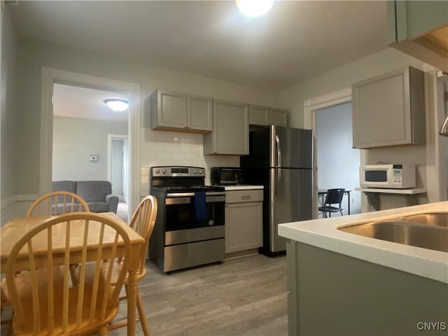 kitchen featuring gray cabinetry, stainless steel appliances, tasteful backsplash, sink, and light hardwood / wood-style flooring