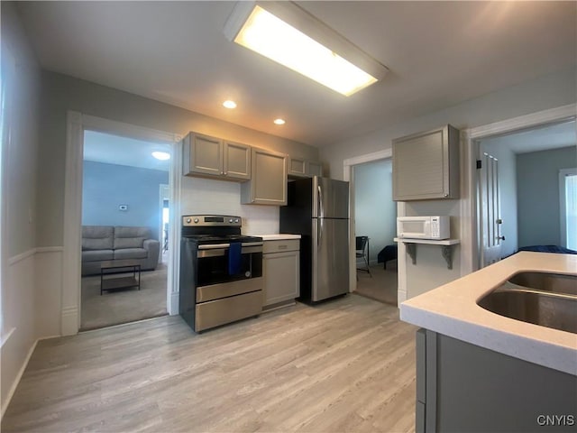 kitchen with backsplash, gray cabinets, sink, light hardwood / wood-style flooring, and appliances with stainless steel finishes